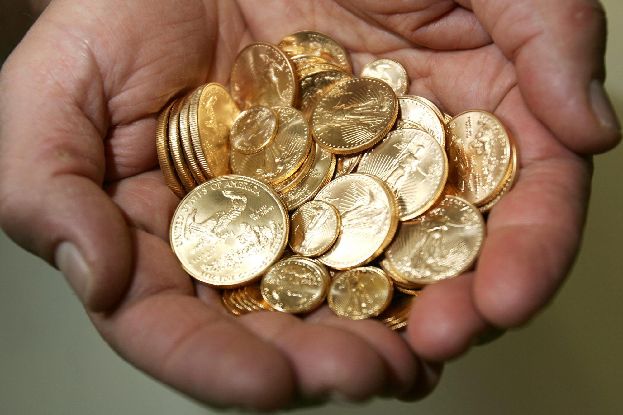 Hands holding stacks of gold coins representing direct purchase of precious metals